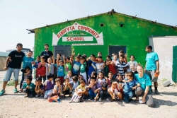 Voluntaris de l'ONG Armando Aid amb els infants del camp d'Oinofyta. Al darrera, l'escola. Autora: Pilar Liberty Munro.