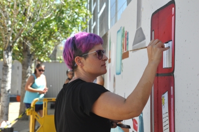 Una mare pintant un mur del pati infantil amb elements de joc simbòlic.